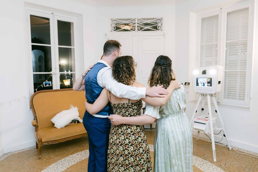 Three people pose together facing a photo booth at an elegant indoor wedding reception venue.