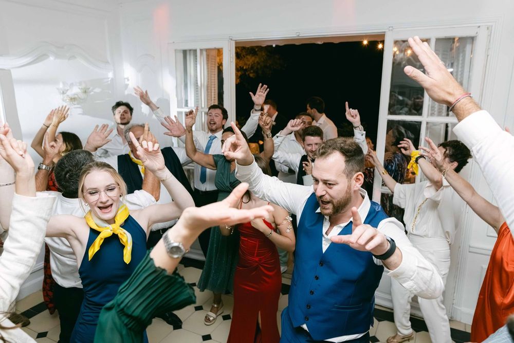 Guests dancing energetically at a lively wedding reception party indoors with raised hands and joyful expressions.