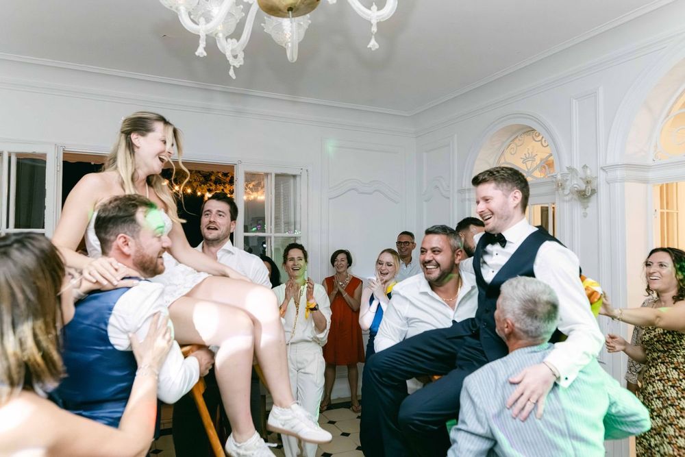 Joyful wedding reception guests lifting bride and groom in elegant ballroom during lively celebration dance party.
