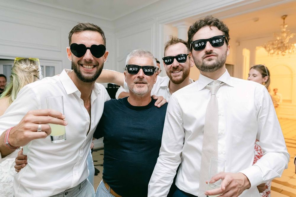 Four men wearing matching black sunglasses posing together at a wedding reception celebration.