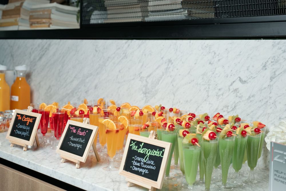 Colorful cocktail drinks displayed on a marble bar with chalkboard signs at an elegant party or brunch event.