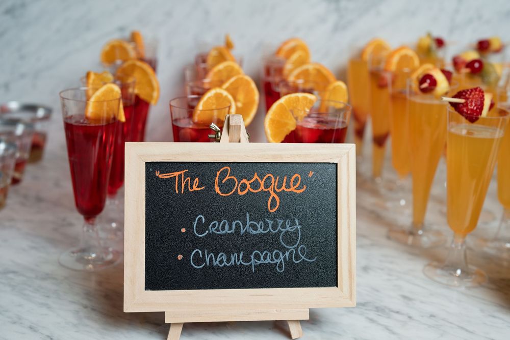 Elegant champagne bar with cranberry mimosas garnished with orange slices and a chalkboard sign reading The Bosque.