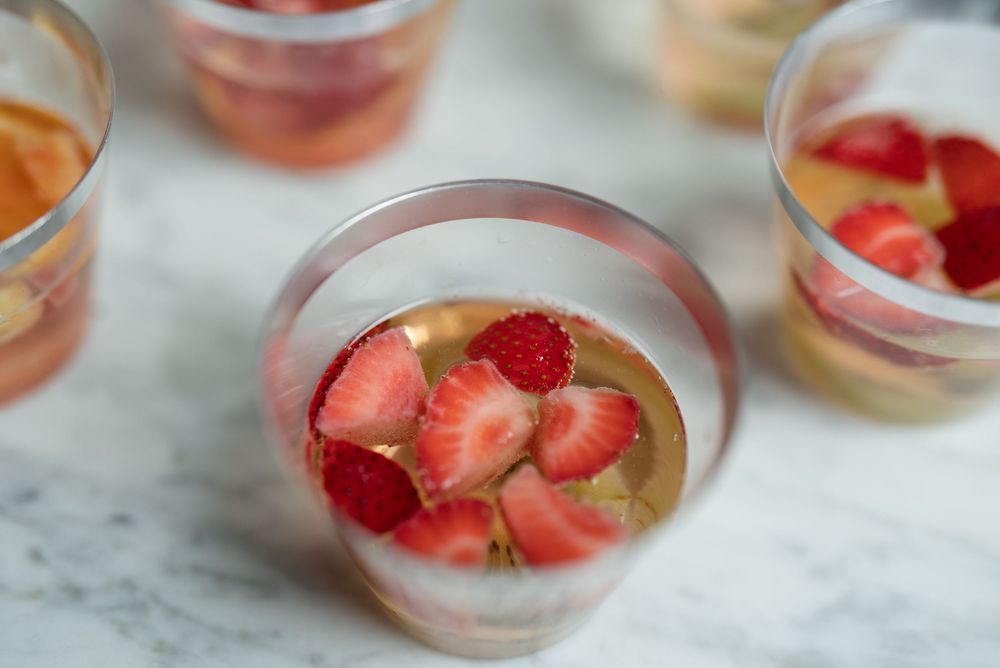 Clear plastic cups filled with fresh strawberries, raspberries, and citrus slices in a light punch on a marble surface.