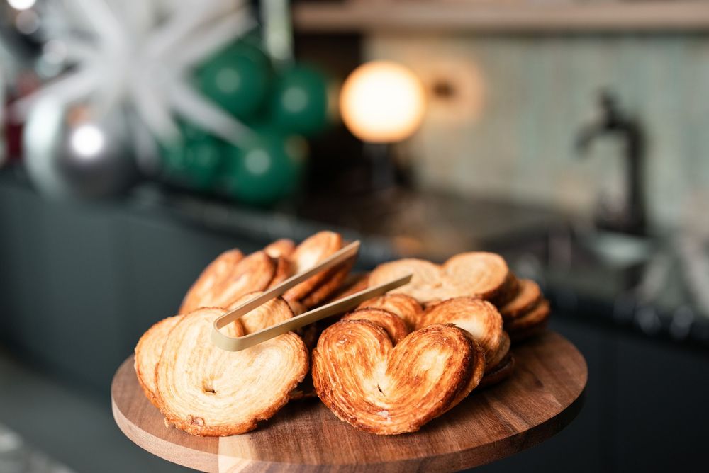 Heart-shaped palmier cookies arranged on a wooden board in a cozy kitchen setting.