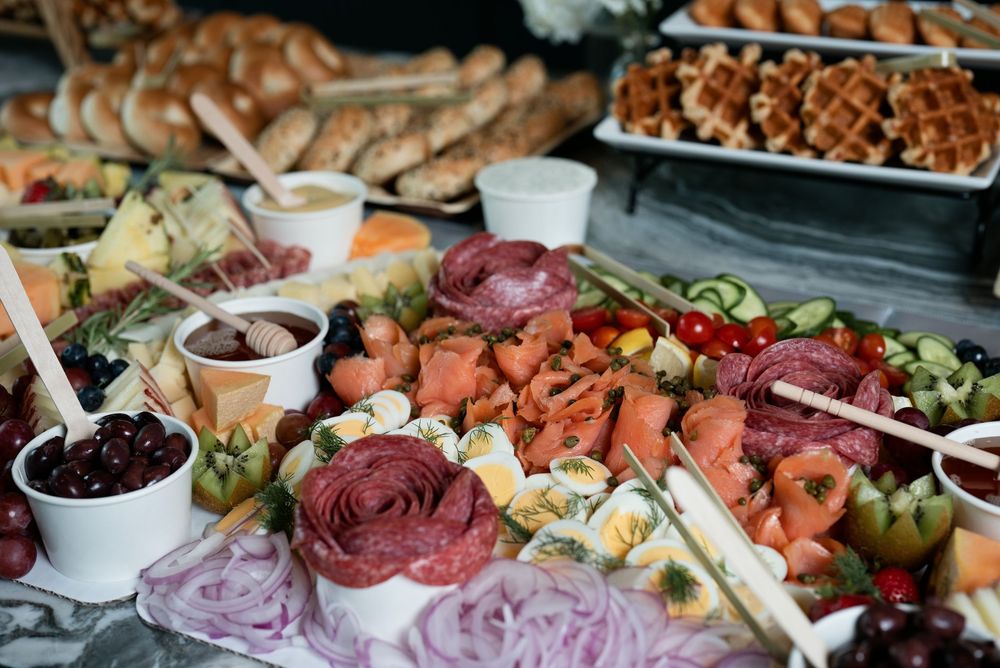 Elegant charcuterie board with smoked salmon, salami roses, cheeses, olives, vegetables, and assorted breads at a catered event.