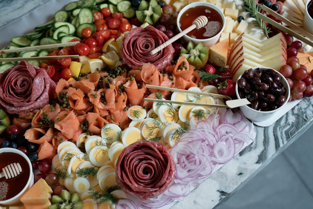 Elegant charcuterie board with salami roses, boiled eggs, melon, tomatoes, olives, cheese, and honey for entertaining.