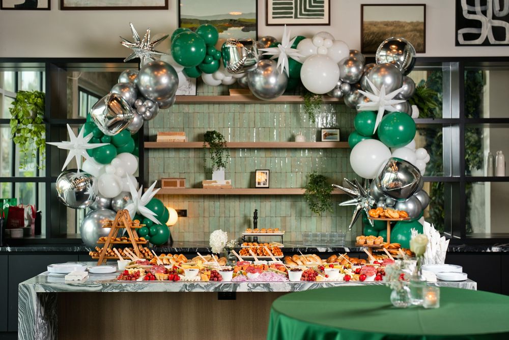 Festive buffet table with green, white, and silver balloon arch decorated with star accents at a party event.