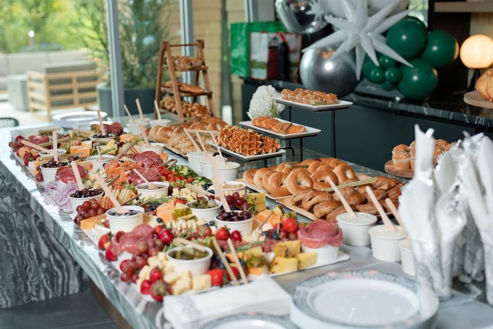 Elegant buffet table with charcuterie, breads, and appetizers at an event with green balloon decor.