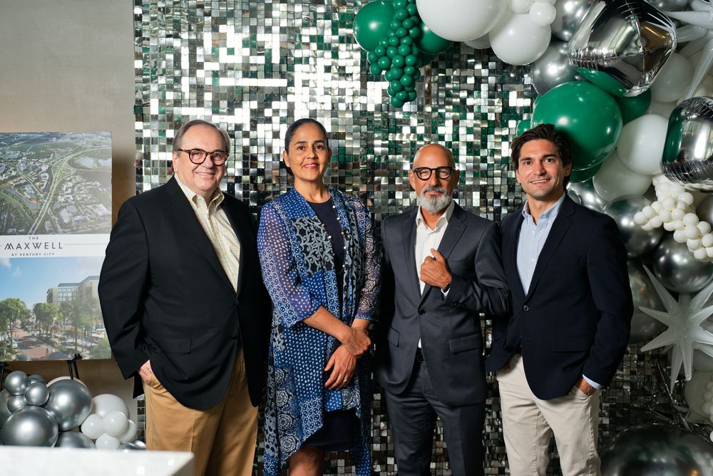 Four professionals smiling together at a celebratory event with green and silver balloon decorations.