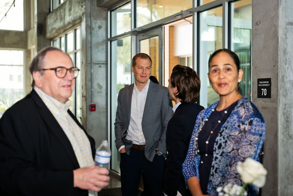 Four professionals networking in a modern building lobby, engaged in conversation near glass doors.
