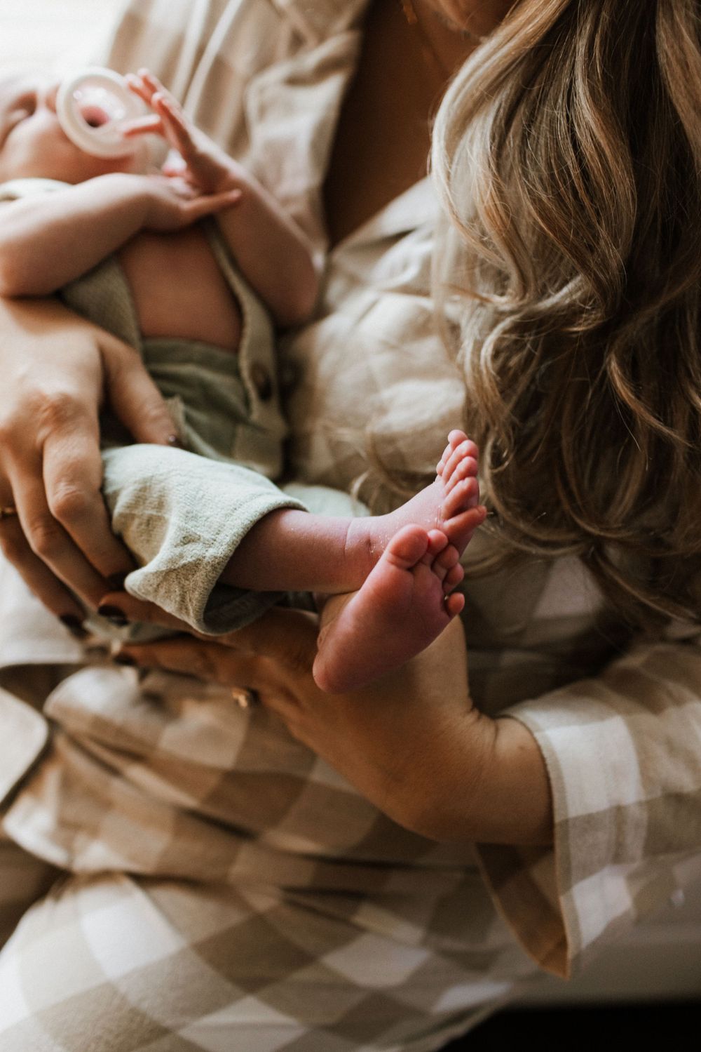 Mother in plaid pajamas cradling a newborn baby, gently holding the infant's tiny pink feet.