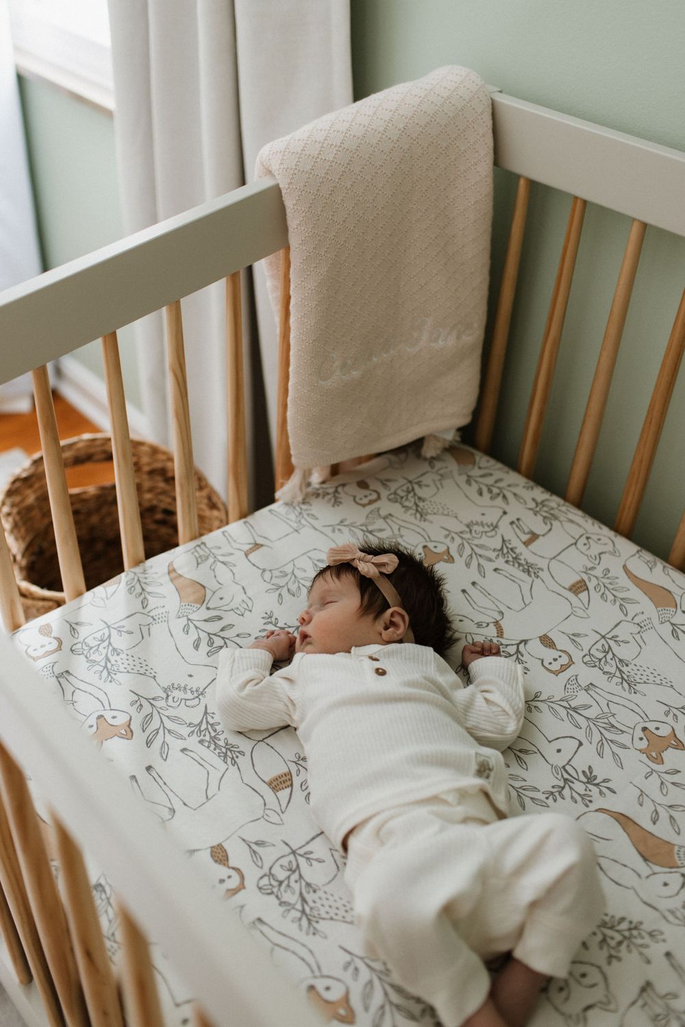 Newborn baby resting in a white wooden crib with animal print sheet.