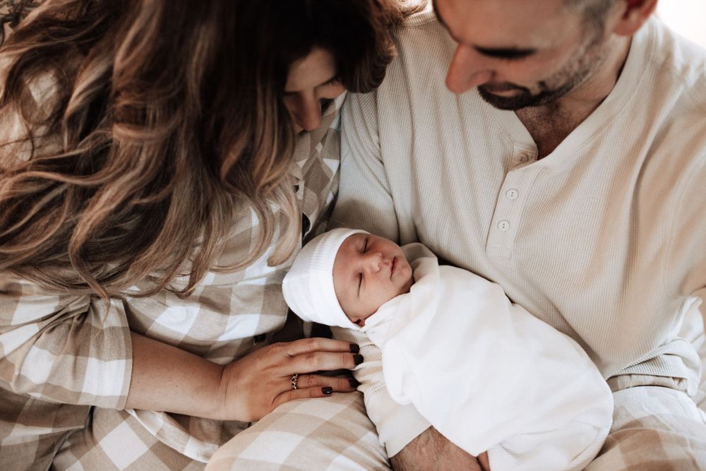 New parents lovingly cradling their swaddled newborn baby together.