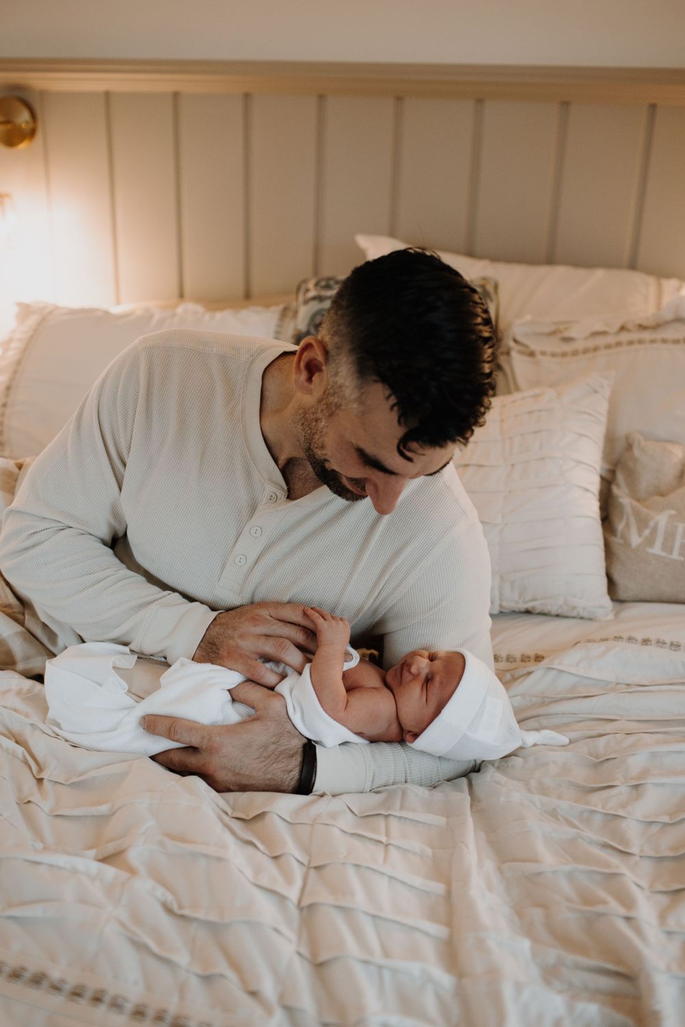 Father lovingly gazing at his newborn baby on a cozy beige bed.