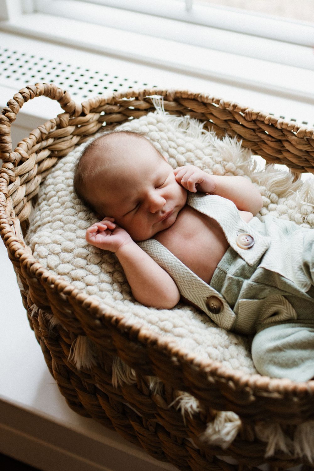 Peaceful newborn baby sleeping in a woven wicker basket by a window.