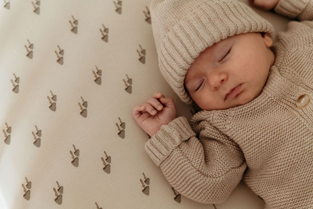 Sleeping newborn baby in beige knit outfit and hat on bunny print blanket.