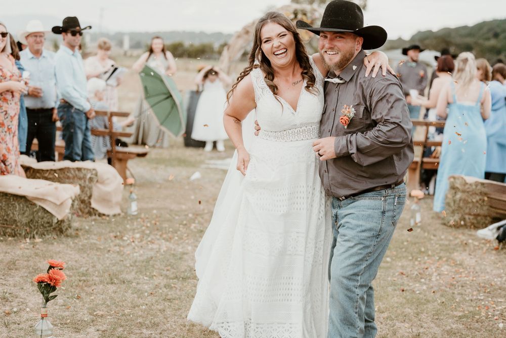 Happy bride and groom walking down outdoor aisle at rustic country wedding celebration.