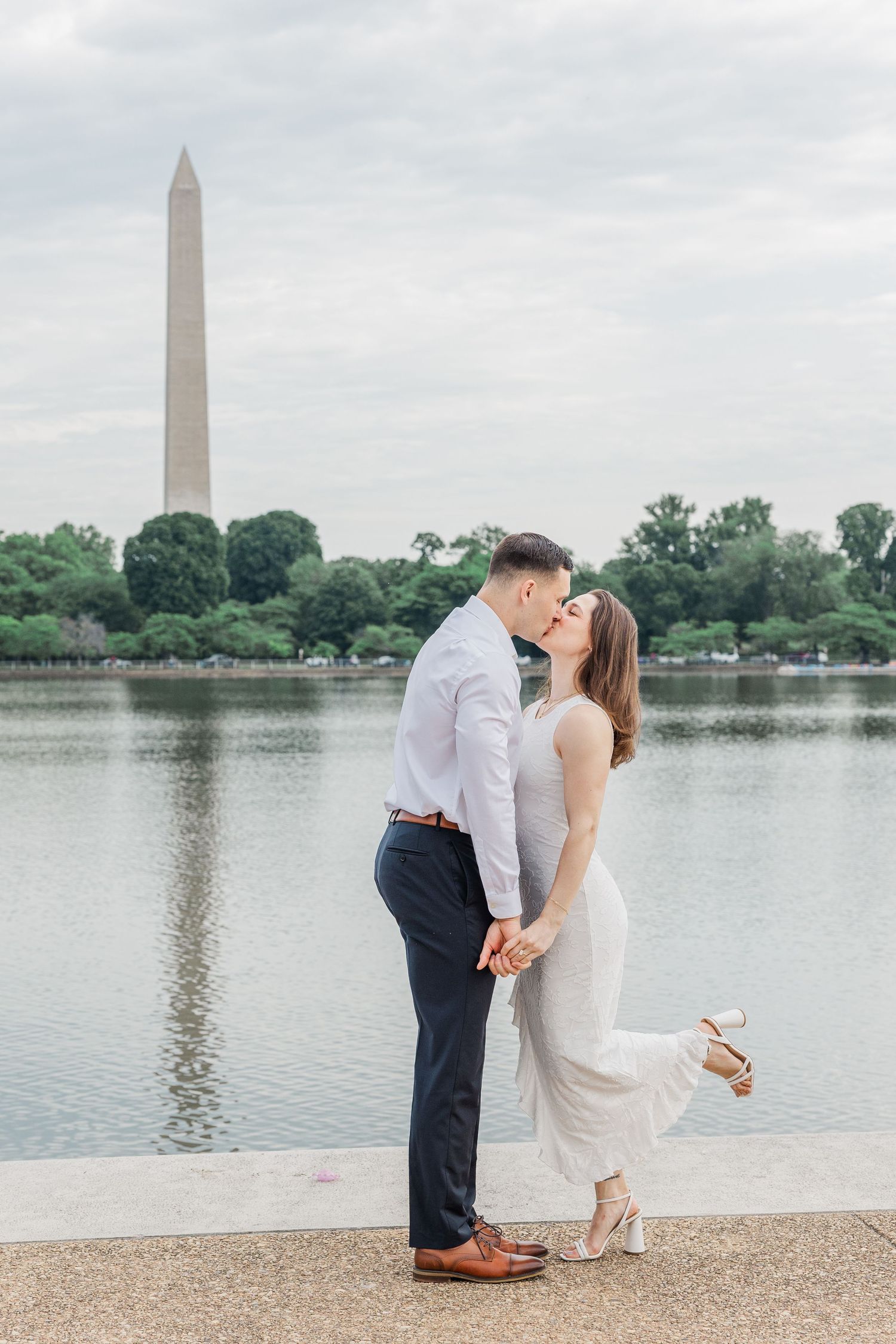 Couple kissing by the Tidal Basin with the Washington Monument reflected in the water behind them.