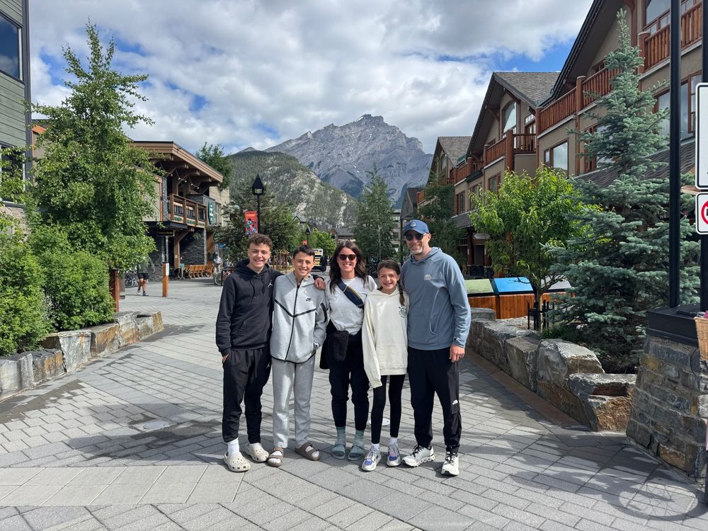 A group of visitors explore a scenic mountain resort area with stone pathways and rustic buildings in the background.