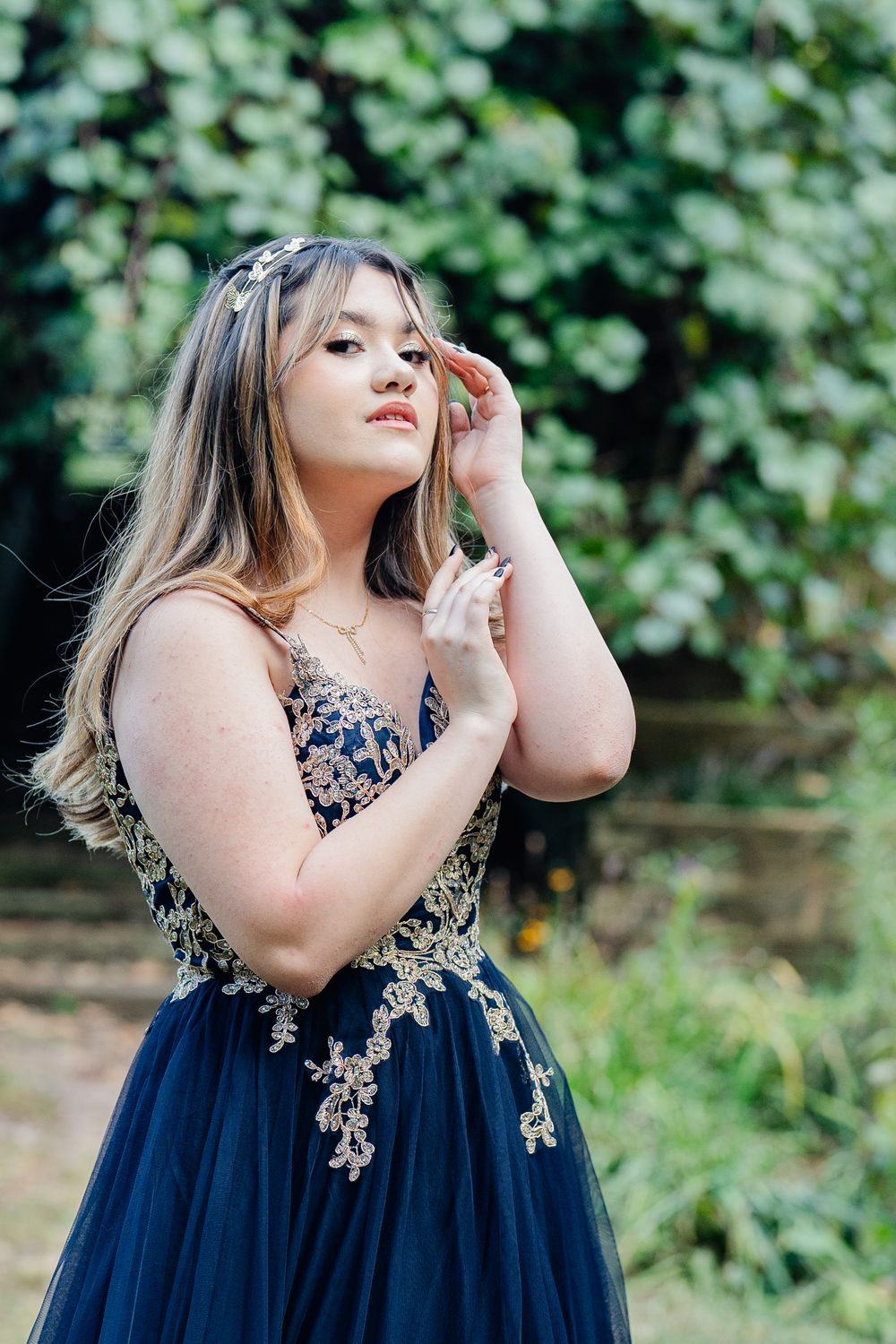 Young woman in navy blue embroidered gown with gold lace details and floral headpiece posing outdoors.