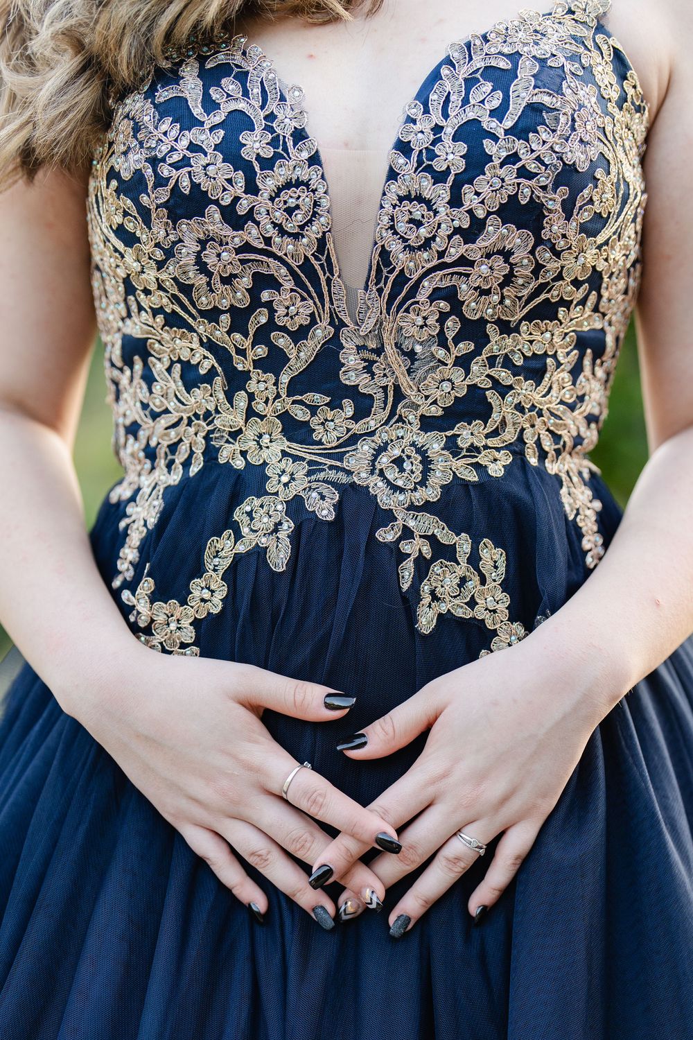 Navy blue prom gown with gold embroidered bodice and deep V-neckline, model posing with hands on waist.