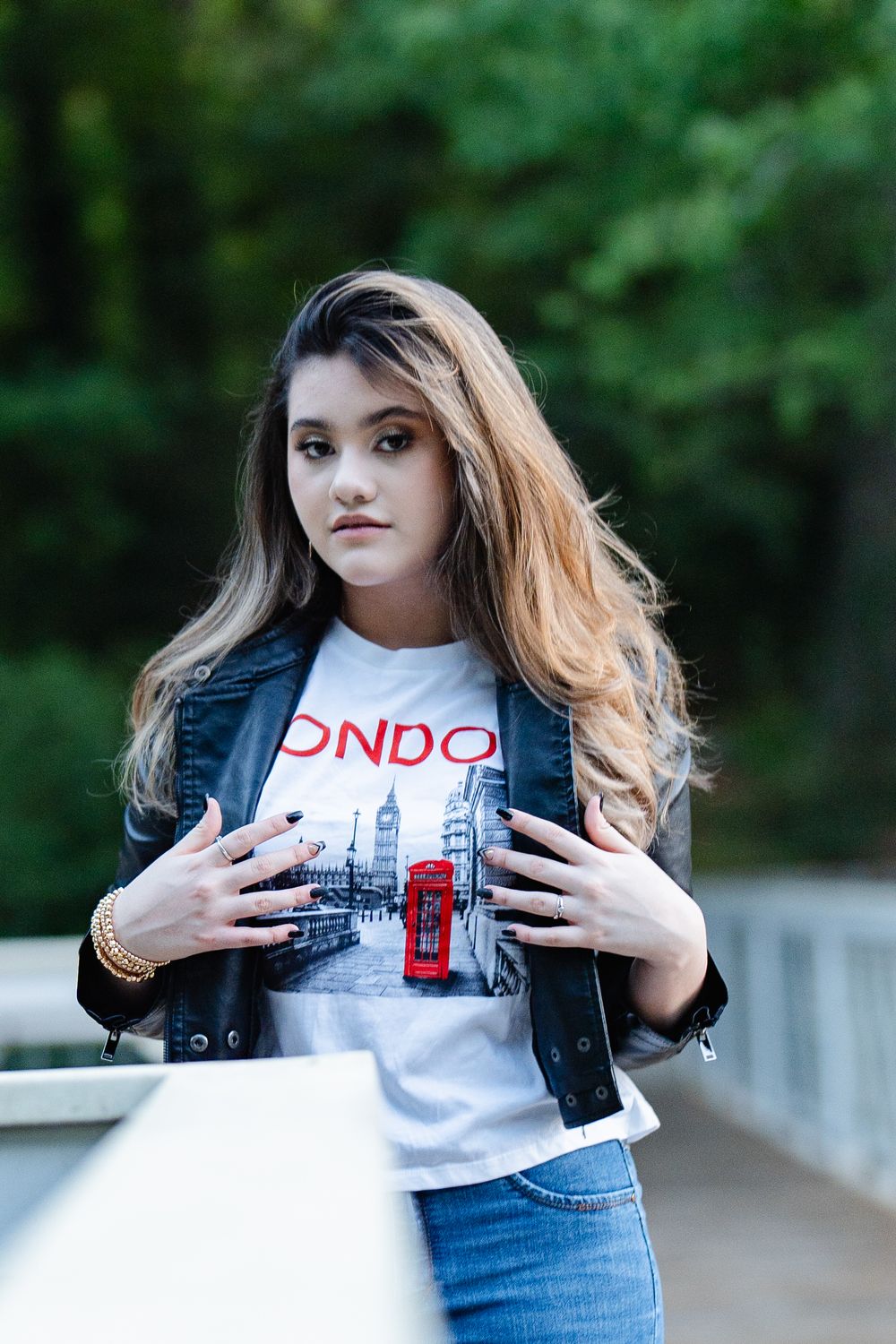 Young woman in London graphic tee and leather jacket posing outdoors.