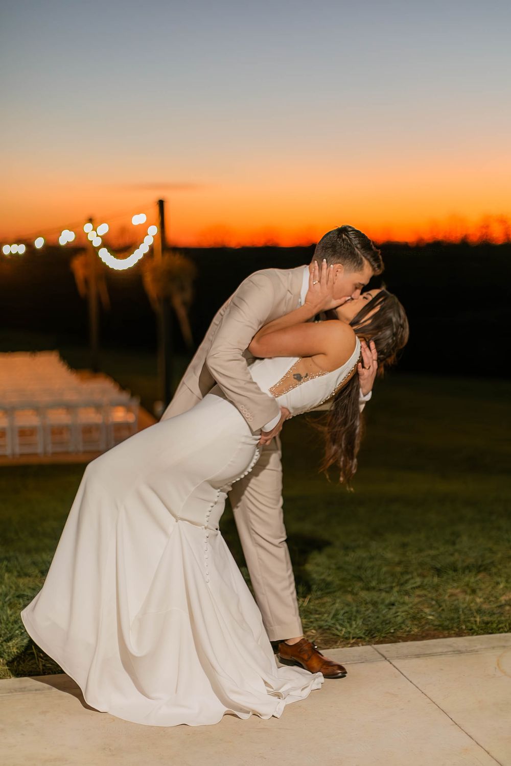 A romantic sunset wedding portrait shows a couple in white sharing an intimate dance dip on an outdoor patio.