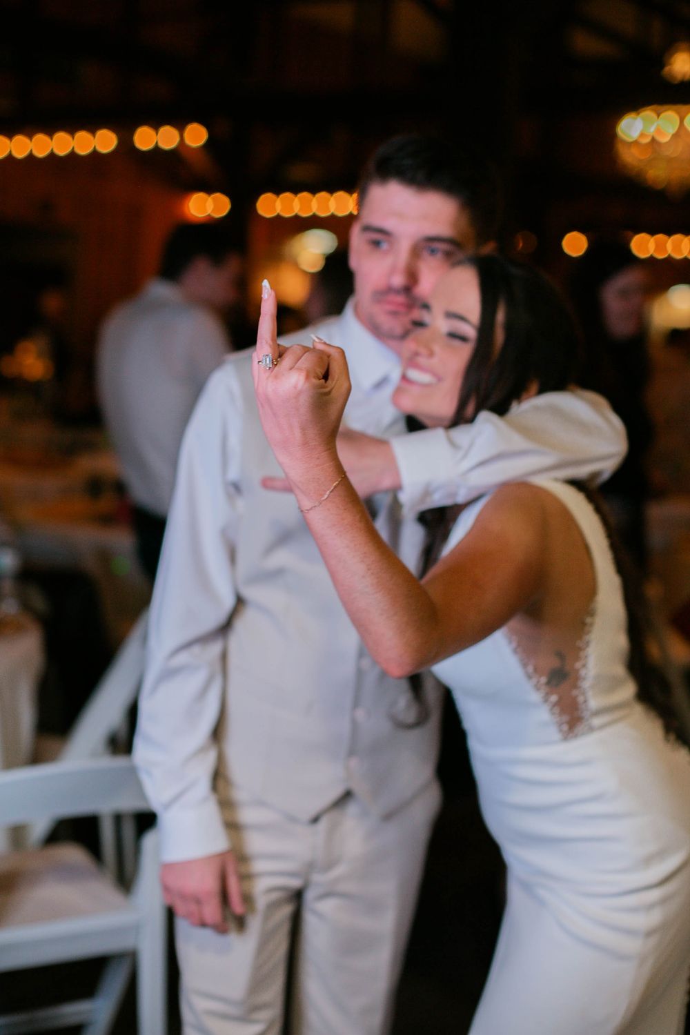 A candid moment under warm lighting during a wedding reception with festive decorations in the background.
