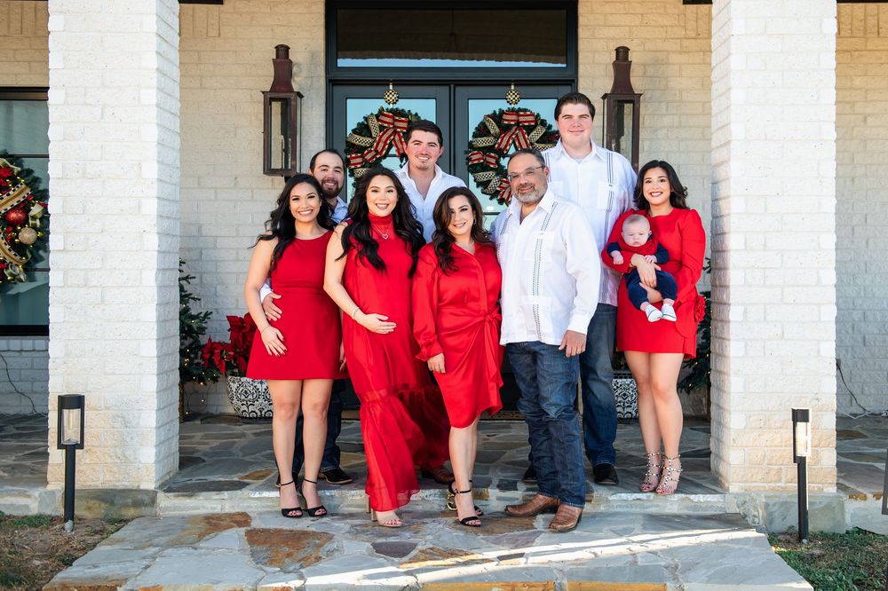 Large family in red and white outfits poses on a front porch decorated with holiday wreaths, including a baby.