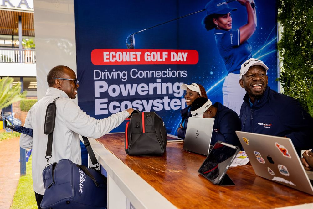 Three men gather at a registration desk with laptops and bags in front of an Econet Golf Day banner about driving connections.