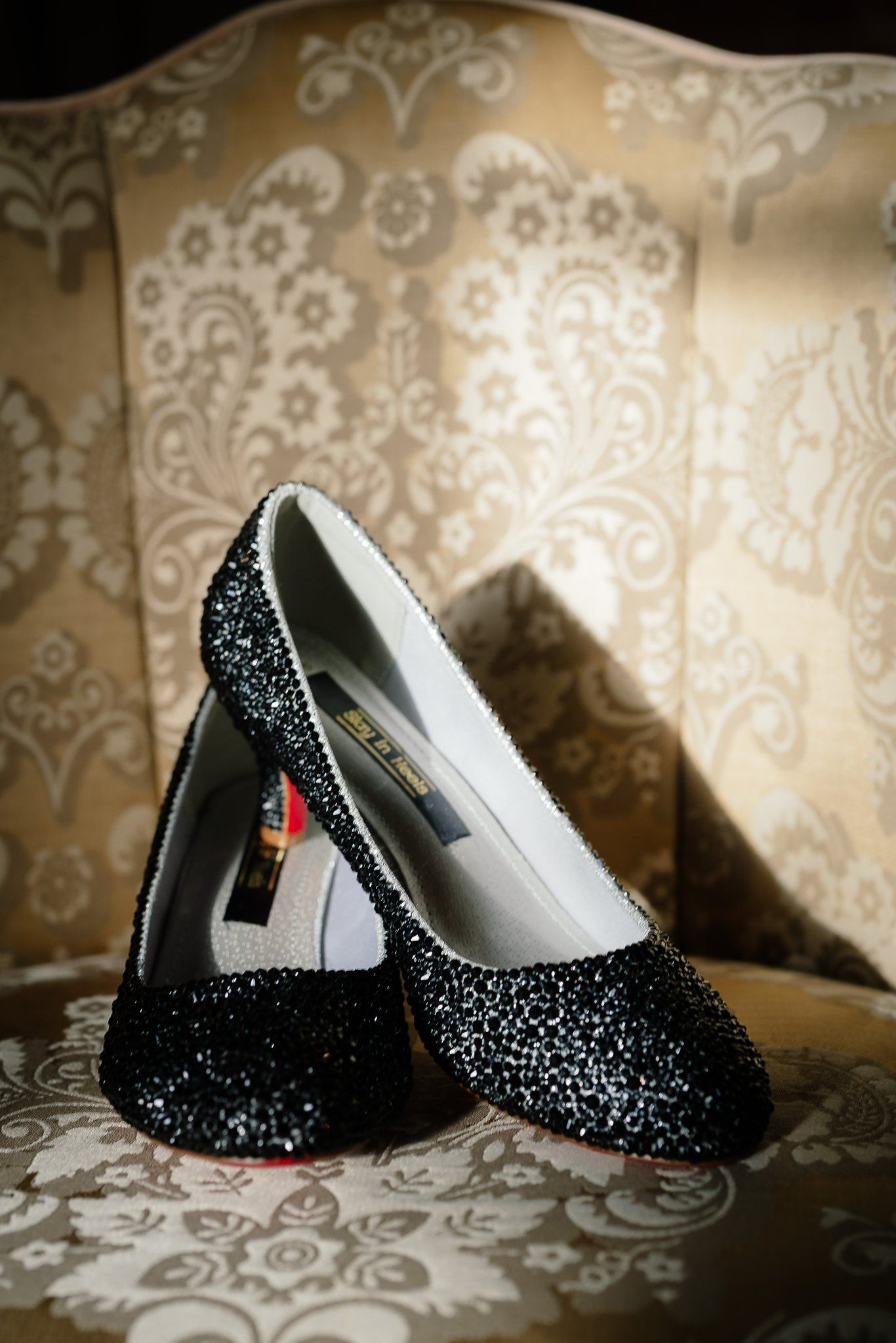 Black glitter wedding shoes with red soles by Slay in Heels on a gold damask chair