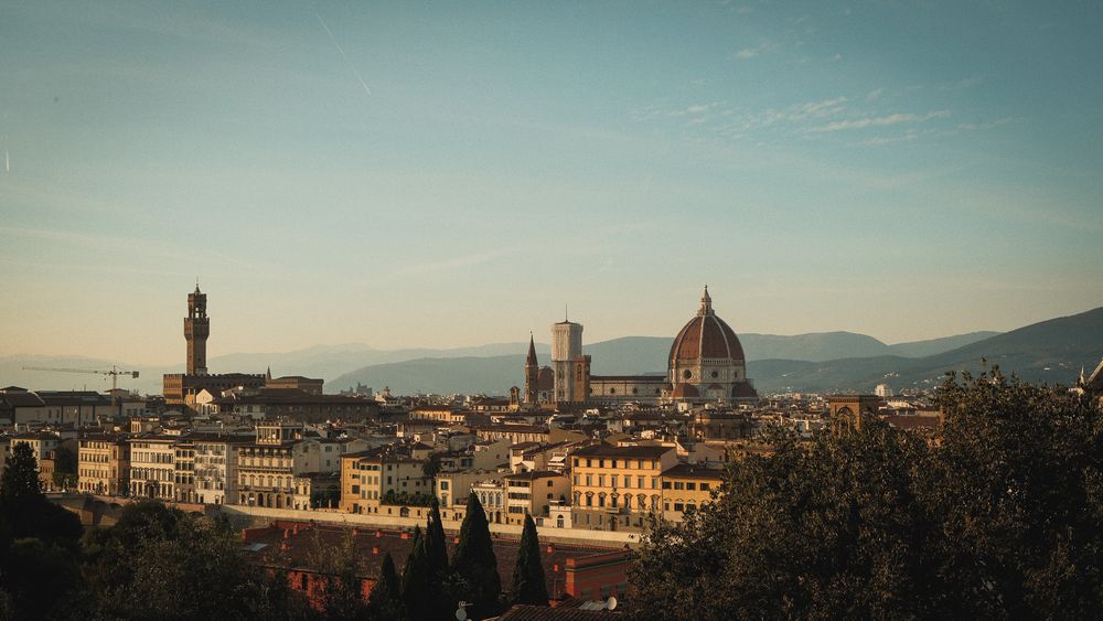 Golden sunset light over the Florence skyline with the cathedral dome, Palazzo Vecchio tower and Tuscan hills in the background.