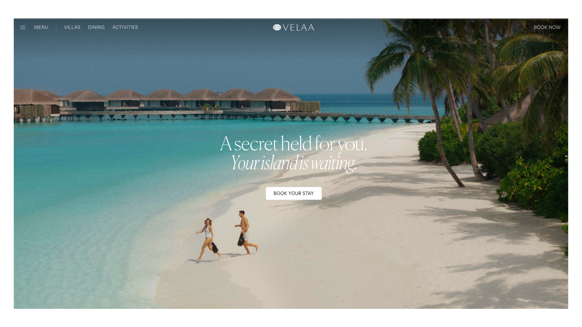 Couple running on a pristine white sand beach with turquoise waters and overwater bungalows at a luxury Maldives resort.