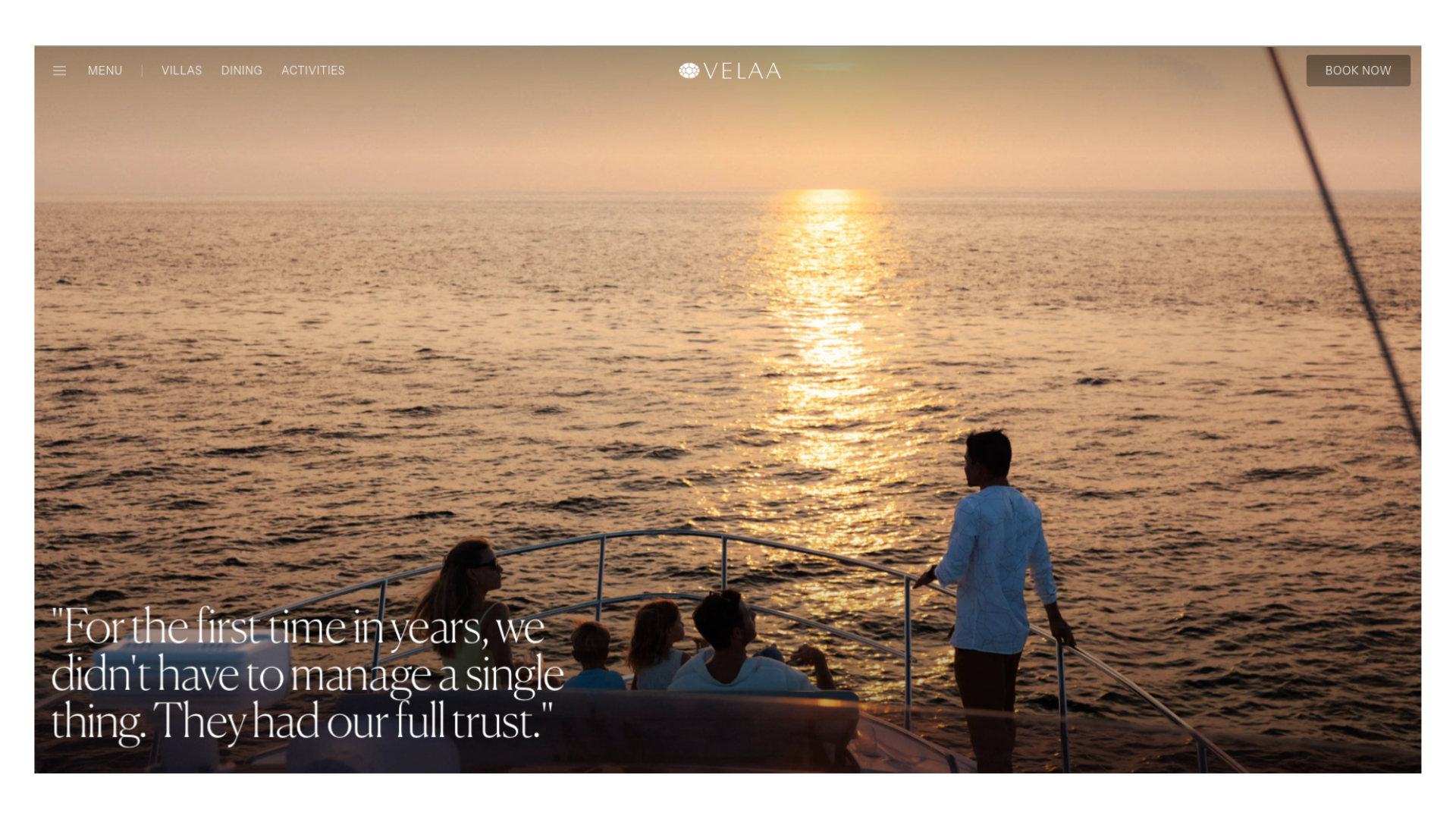 Silhouettes of people on a sailboat deck watching a golden sunset over calm ocean waters.