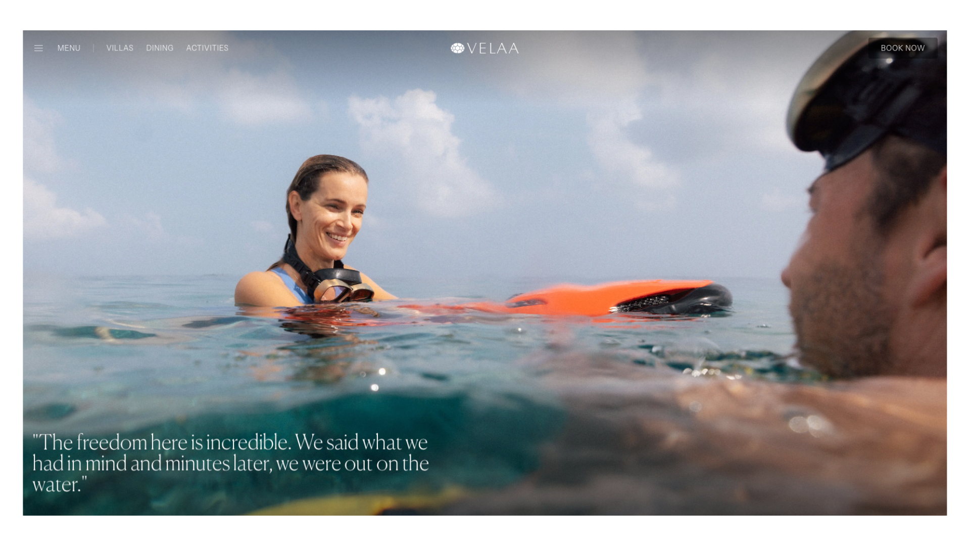 Two surfers smile at each other while floating on surfboards in calm tropical ocean waters.