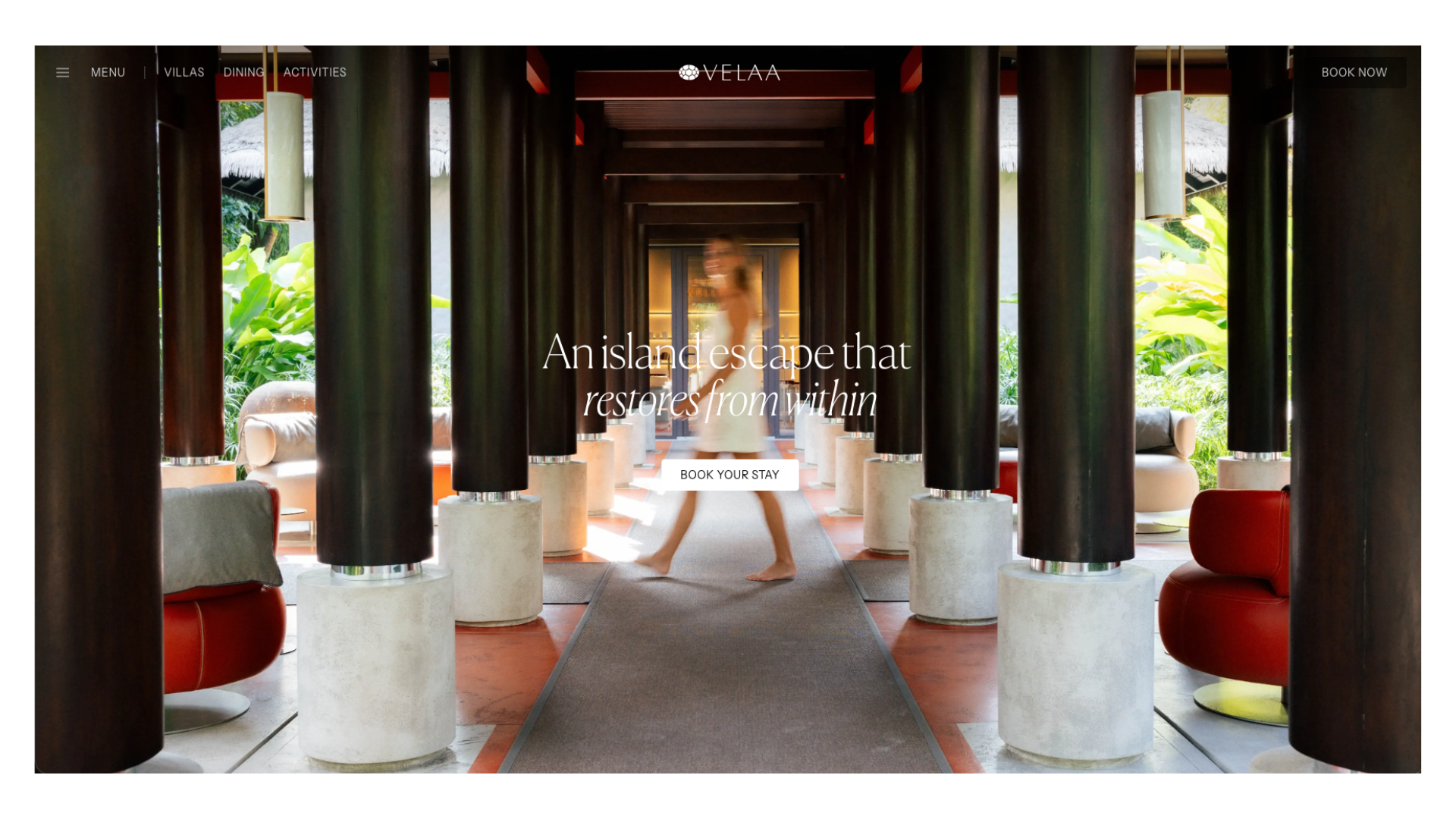 Luxury resort corridor with elegant columns, lush tropical greenery, and stylish red accent chairs creating a serene island escape.