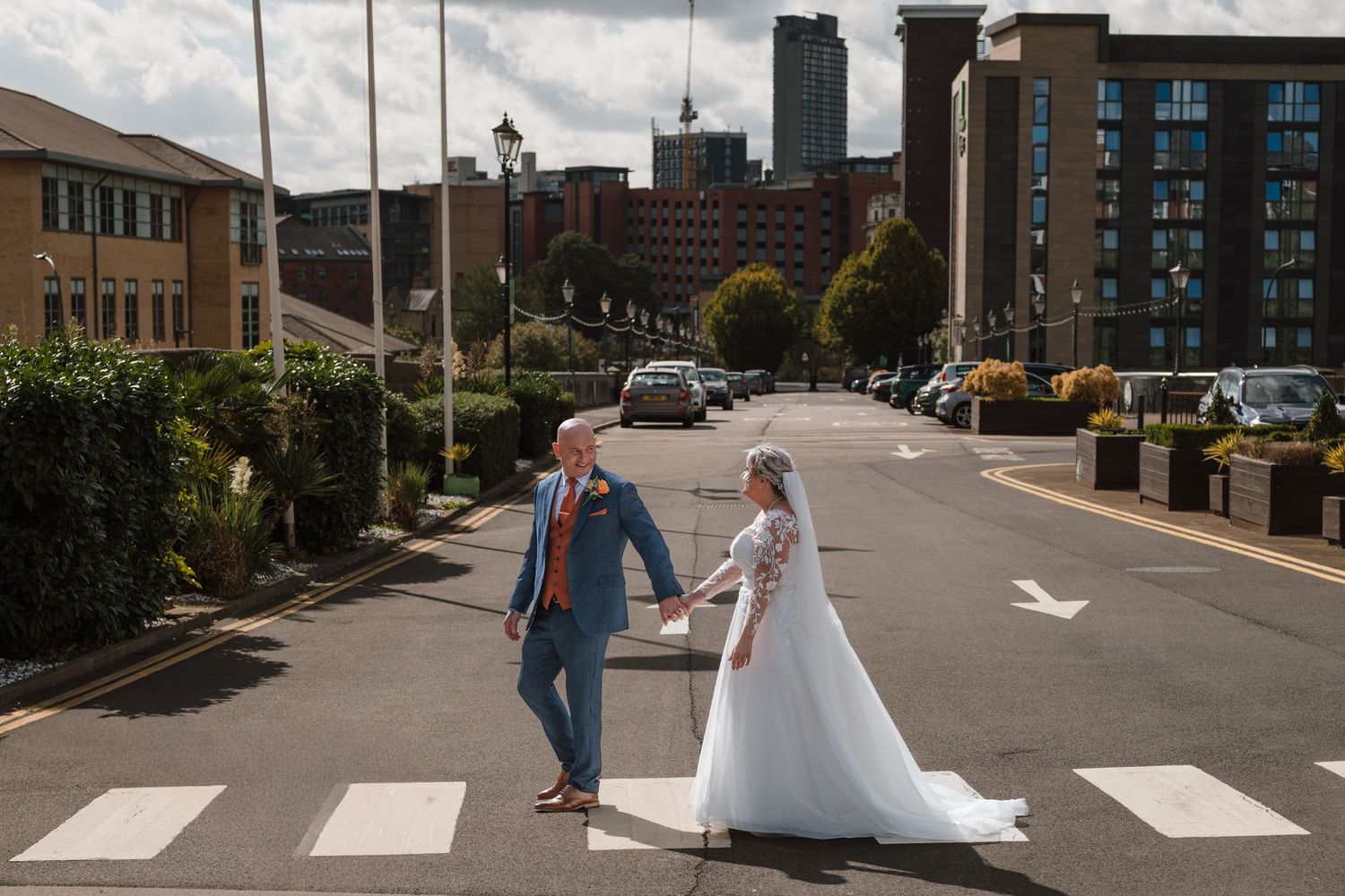 Bride and groom hold hands on a zebra crossing in an urban city street setting on their wedding day.