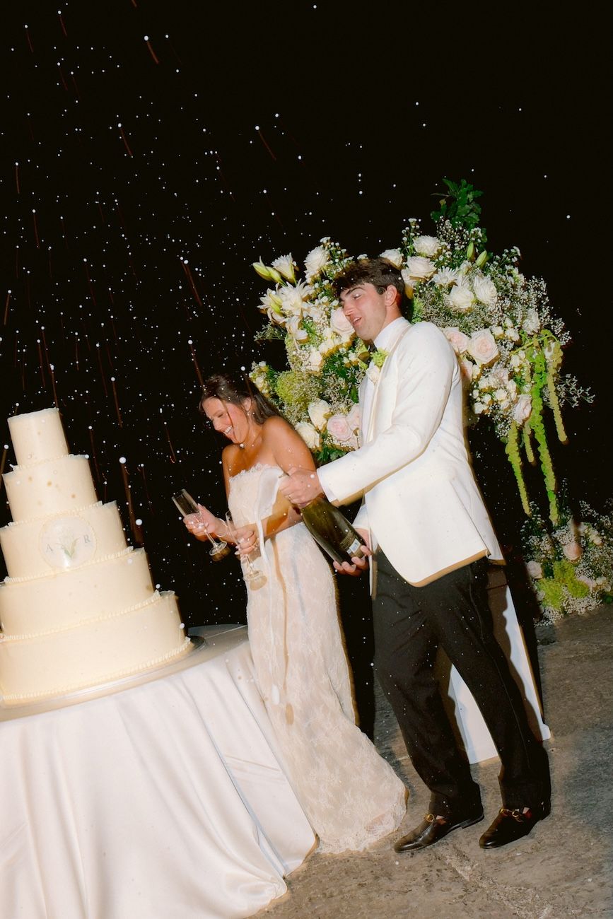 Cheerful bride and groom opening the champagne during the cake moment of their destination wedding at Villa Bettoni, Lake Garda, Italy.