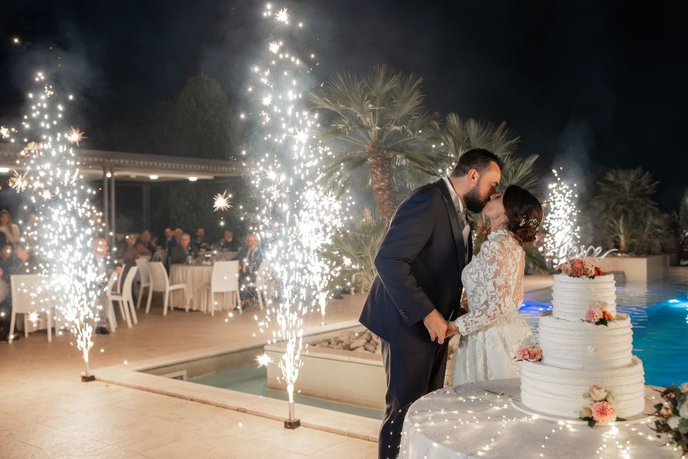 Antonio e Maddalena si baciano accanto alla torta, tra scintille e luci della piscina.