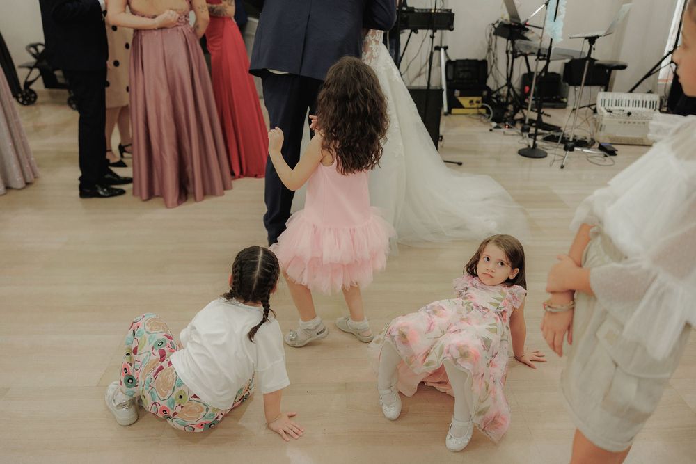 I bambini giocano sul pavimento durante la festa, tra gonne e abiti degli invitati.