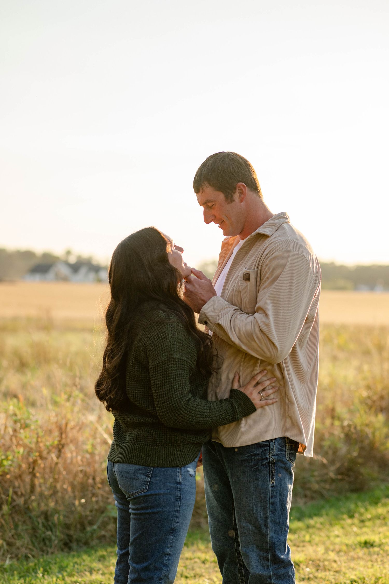 Couple shares tender moment at golden hour in open field with warm backlit sunset glow.