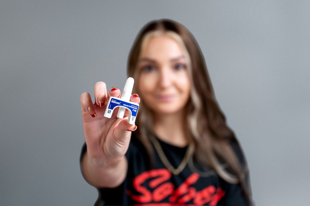 Woman in black Sober shirt holds small nasal spray bottle toward camera.