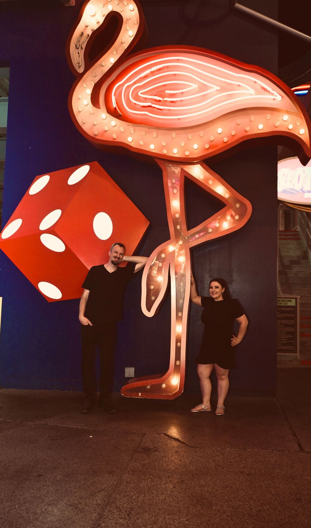 Couple posing in front of illuminated flamingo sign and red dice decoration in Las Vegas.