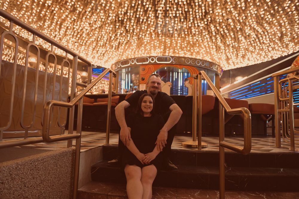Couple posing under stunning golden light ceiling at an elegant casino venue with brass railings.