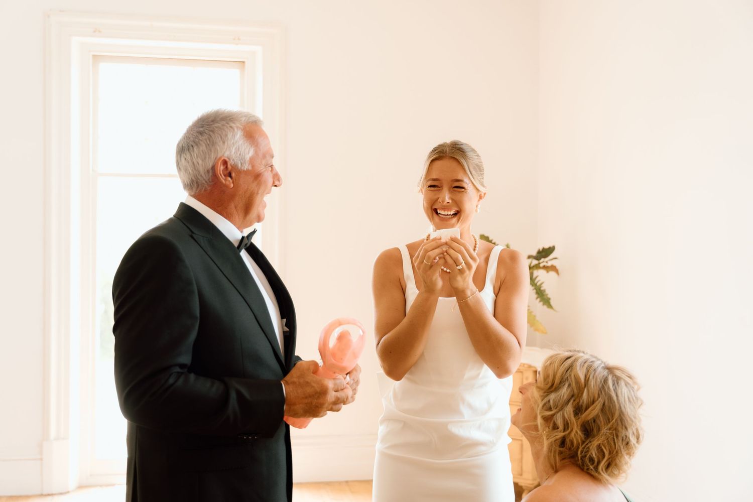 Bride in white dress laughing with elderly man in tuxedo at wedding celebration indoors.