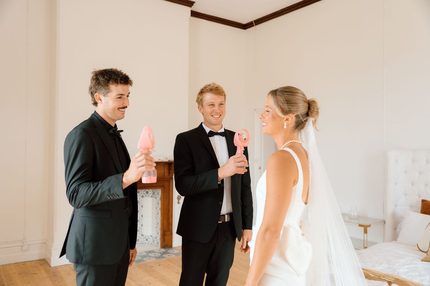 Bride and two groomsmen in tuxedos sharing a joyful moment with pink ice cream cones indoors.