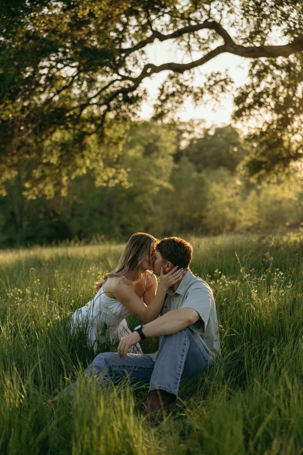 A couple shares a romantic kiss while sitting in a lush green meadow during their engagement session in Georgia.