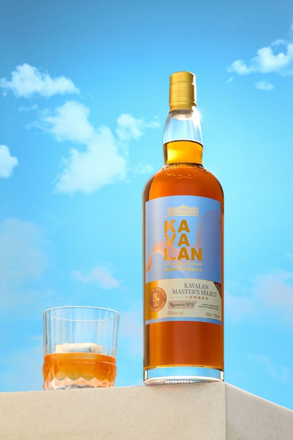 Kavalan Master's Select whisky bottle beside a glass with ice, set against a bright blue sky with clouds.