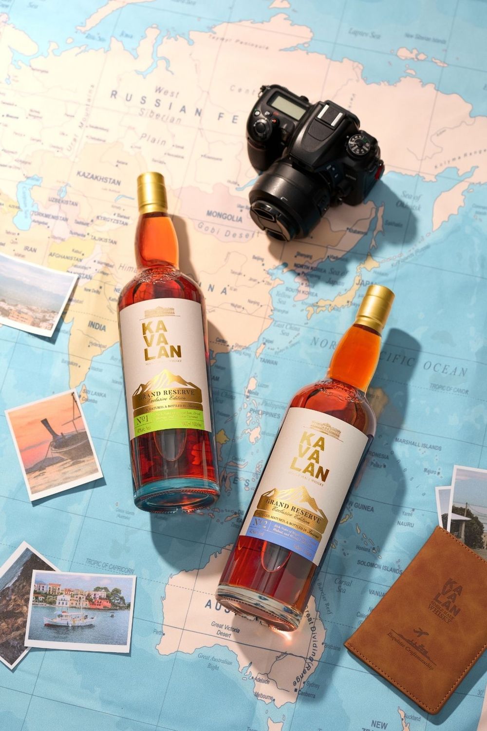 Two Kavalan whisky bottles displayed on a world map with a camera, postcards, and passport for travel-themed product shot.