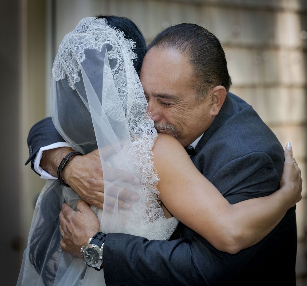 A bride in a white veil shares a heartfelt hug with an older man in a suit at a wedding ceremony.